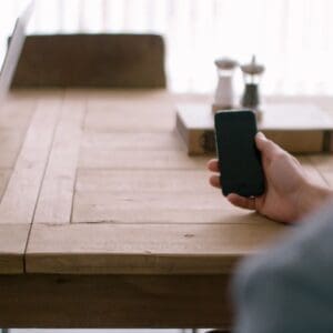 A person holding a cell phone on top of a wooden table.