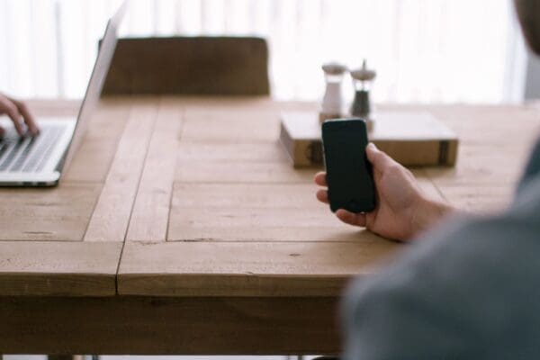 A person holding a cell phone on top of a wooden table.
