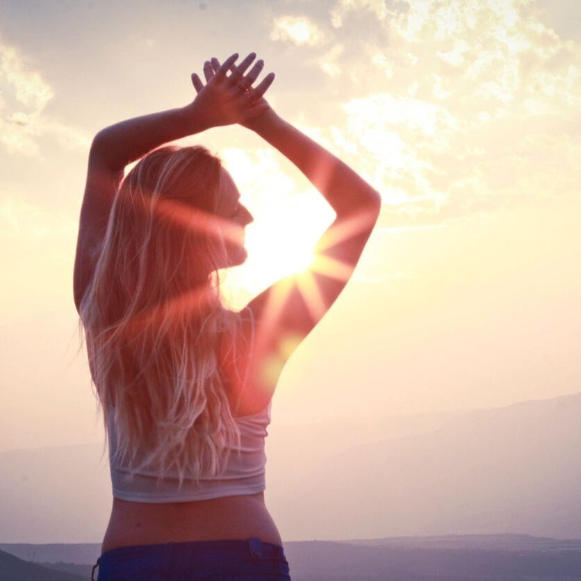 A woman is standing in the sun with her hands up.