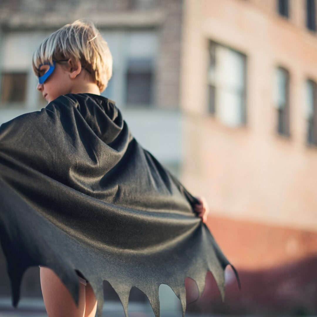 A young boy wearing a batman cape and mask.