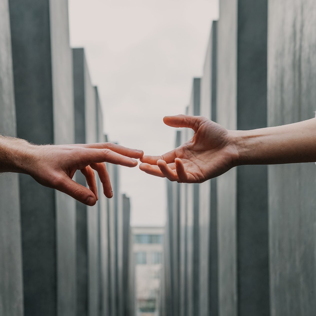 Two hands reaching out to each other in a line of concrete buildings.